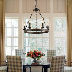 a chandelier hangs over a dining room table with plaid chairs and flowers on it