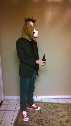 a man wearing a horse mask and holding a beer in his hand while standing next to a wall