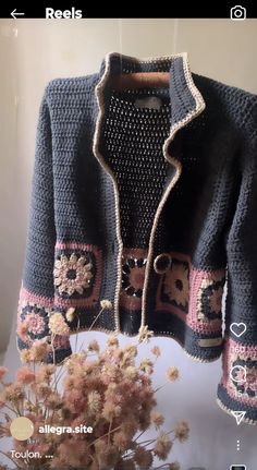 a crocheted jacket with flowers and hearts on the front is hanging from a hook