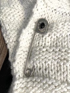 a white knitted sweater with a button on the lapel and a metal hook attached to it