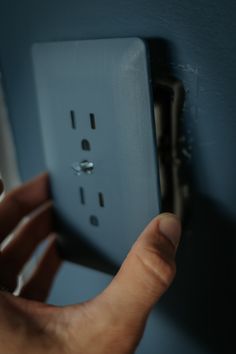 a person is holding an electrical outlet in their left hand and pressing it on the wall