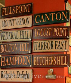 several wooden signs mounted to the side of a building that says, fell's point, mount vernon, federal hill, locus point, fulton, harbor east, hamper