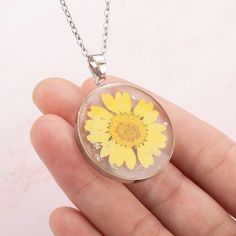 a person holding a glass pendant with a yellow flower on it's back end