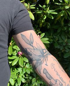 a man with a tattoo on his arm holding a cell phone in front of some bushes