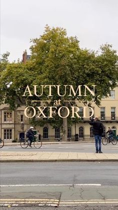 people riding bicycles on the street in front of an old building with autumn at oxford sign