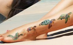 a woman laying on the beach with her legs covered in tattoos and sea turtle designs