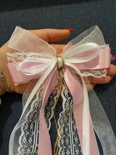 a woman's hand holding a pink ribbon with white lace and bows on it