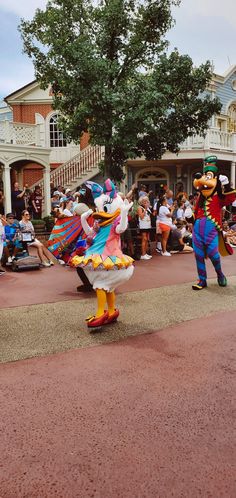 two mickey and donald mouse characters dancing in front of a group of people on the street