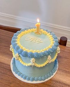 a blue and yellow cake with a single candle on it sitting on a wooden table