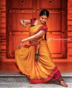 a woman in an orange and red sari dancing on the steps with her arms outstretched