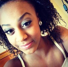 a close up of a woman with curly hair and blue eyeshadow smiling at the camera