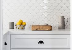 a kitchen with white cabinets and marble counter tops, along with two bowls of lemons