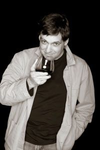 a man holding a glass of wine in his right hand and looking at the camera