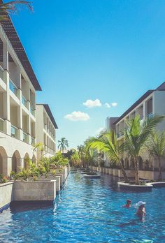 two people are swimming in the pool next to an apartment building and palm trees on either side