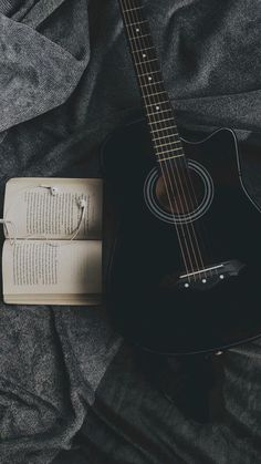 an open book and guitar laying on top of a bed next to it's strings