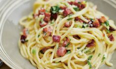 a plate of pasta with bacon and parsley on the top is ready to be eaten