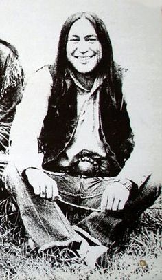 an old photo of two people sitting in the grass together, one is smiling and the other has long hair