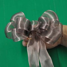 a hand holding a silver bow on top of a green surface