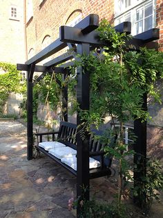 a black bench sitting under a pergoline covered arbor in front of a brick building