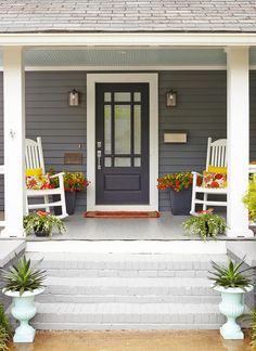 the front porch is decorated with white rocking chairs and potted plants