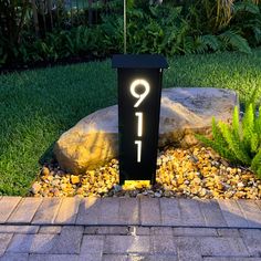 a lit up sign sitting in the middle of a garden next to rocks and plants