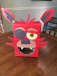 a red box with an animal's face cut out of it on top of a wooden table