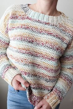 a woman is wearing a multicolored sweater and has her hands in her pockets