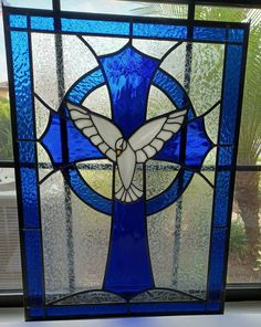 a blue stained glass window with a white dove on it's side and palm trees in the background