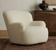 a white chair sitting on top of a rug next to a wooden dresser and lamp