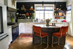 two red chairs sitting at a kitchen island in front of a stove top oven and refrigerator