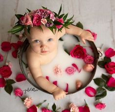 a baby sitting in a tub with flowers on it's head, surrounded by pink roses