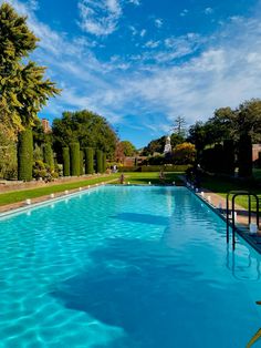 an empty swimming pool in the middle of a park with trees and bushes around it