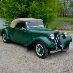 an old green car is parked in the gravel