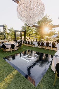 an outdoor wedding reception setup with chandelier and black tablecloths on the grass