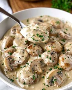 a white bowl filled with mushrooms and gravy on top of a wooden table