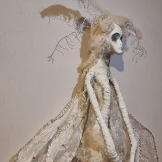 a stuffed animal with long hair and wings on it's head, standing in front of a white wall