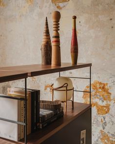 a shelf with books, vases and other items on it in front of a wall