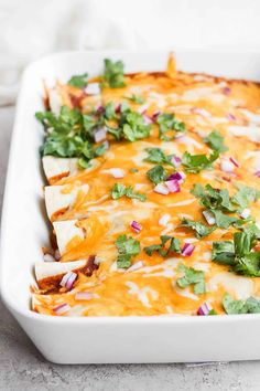 a white casserole dish filled with mexican food and garnished with cilantro