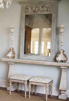 a mirror and two stools in front of a wall with a chandelier