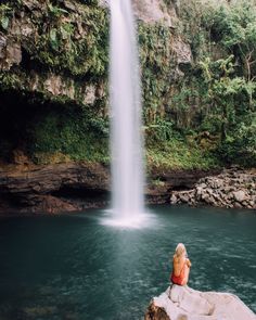 a woman sitting on top of a rock next to a waterfall