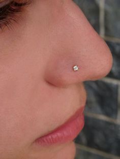 a woman's nose with a tiny diamond in the middle of her nose and a brick wall behind her