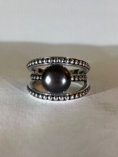 This Single Tahitian Black Pearl and Sterling Ring, which was purchased in Aspen, Colorado in the late '90s, is simply stunning.  The two larger outer sterling silver bands superbly showcase the smaller middle band with the black pearl ... it's as if it was designed to be like a clam sham, slightly open to reveal the surprising pearl inside. The beaded decor on all three bands elevate the modern design. The luster of this Tahitian South Sea pearl is beautiful. Truly a lovely ring to treasure for Beaded Decor, The Black Pearl, Silver Bands, Tahitian Black Pearls, Aspen Colorado, Sea Pearl, Late 90s, South Sea Pearls, Sea Pearls