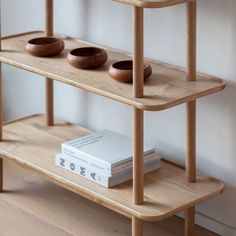 a wooden shelf with three bowls on it and a book in front of the shelves