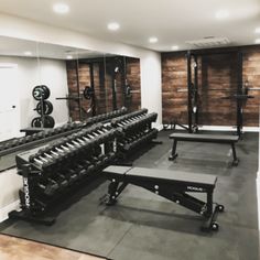 an empty gym room with benches and weight machines on the wall, in front of mirrors