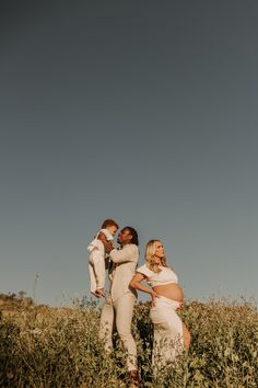 two women and a baby are standing in the tall grass with their arms around each other