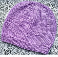 a purple knitted beanie sitting on top of a white and black polka dot blanket