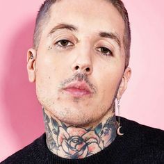 a man with tattoos and piercings on his neck looks at the camera while standing in front of a pink background