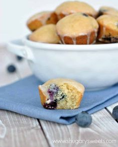 blueberry muffins in a white bowl on a blue napkin next to some blueberries