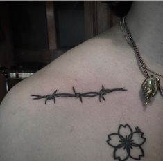 a woman's back with barbed wire and a flower tattoo on her left shoulder