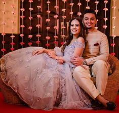 a man and woman are sitting on a chair in front of some string lights with flowers hanging from the ceiling